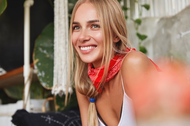 Photo of pleased dreamy beautiful young blonde female student wears bandana on neck