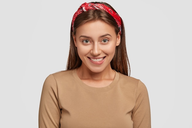 Photo of pleased young female model with toothy expression, looks joyfully