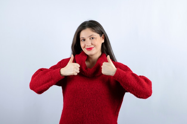 Photo of a pleased young woman in red sweater showing thumbs up