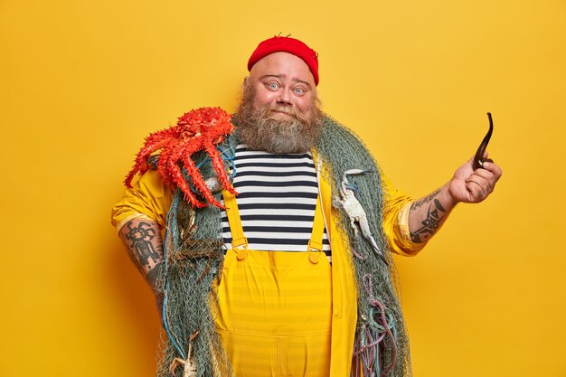 Free photo photo of positive boatswain poses with ocotpus, enjoys marine life, spends much time at boat together with whole crew, holds smoking pipe