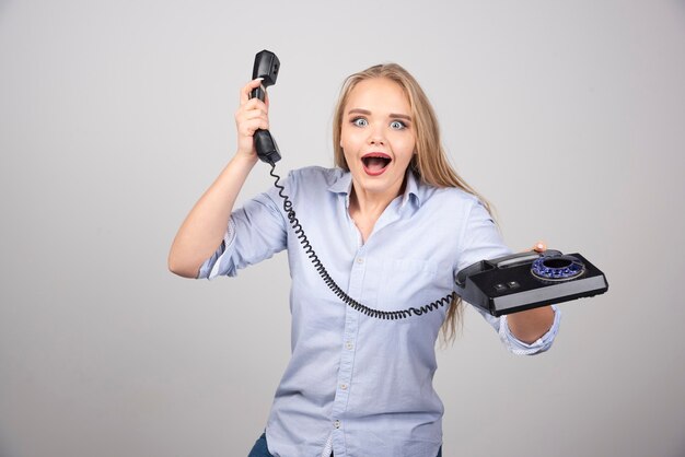 Photo of a positive woman model standing and holding black old handset