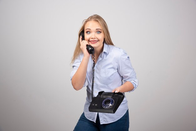 Photo of a positive woman model standing and talking on black old handset