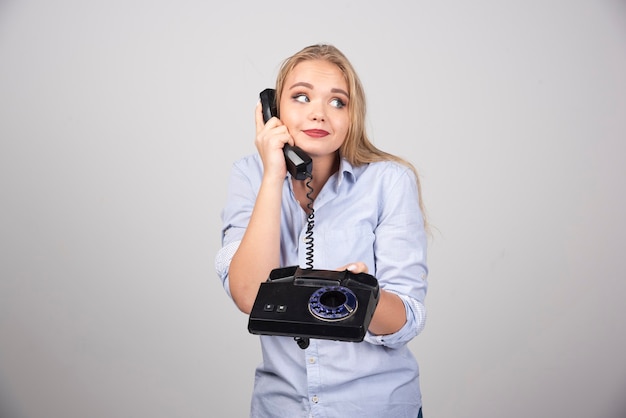 Фотография модели красивой женщины, стоящей и говорящей на черном старом телефоне