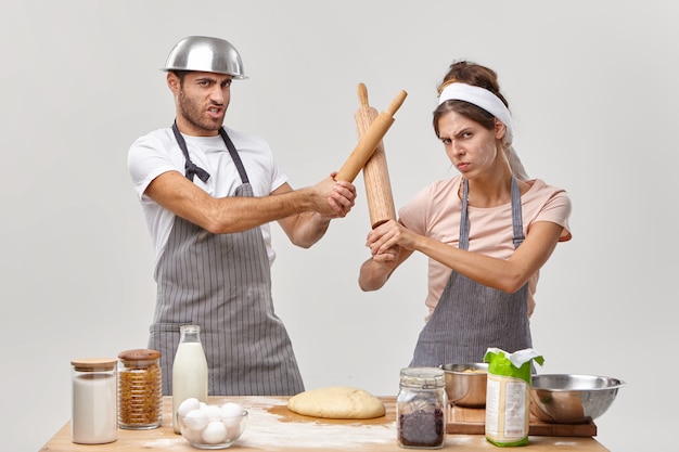 Free photo photo of professional cooks have battle at kitchen, participate in culinary contest, fencing with rolling pins, prepare fresh dough for baking pie, make cookie dessert. chef contest who is best