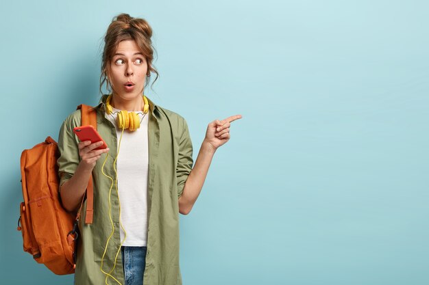 Photo of puzzled young woman holds cellular, updates application for listening favourite song from playlist