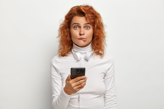 Photo of redhead female bites lips, looks surprisingly at camera