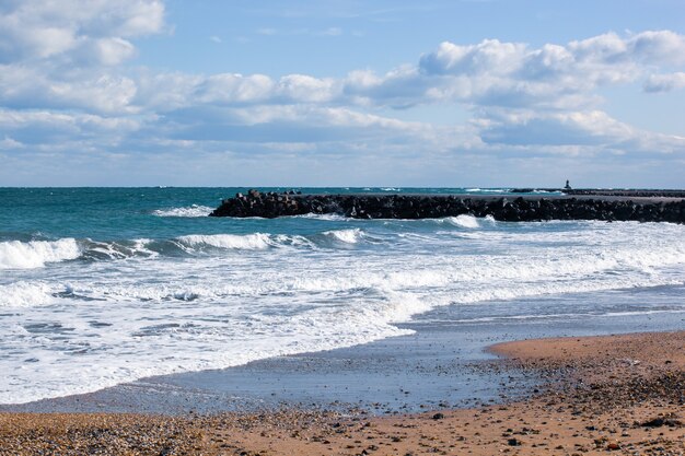 Фотография расслабляющих океанских волн на берегу с каменной пристанью под пасмурным небом