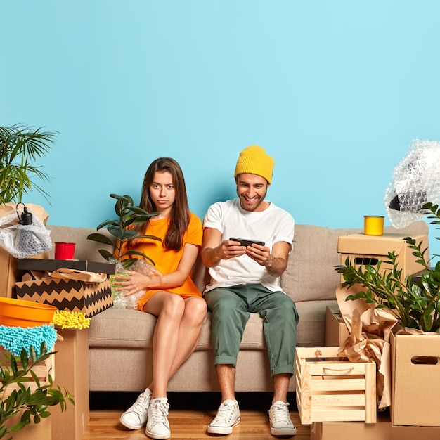 Photo of sad young couple sitting on the couch surrounded by boxes