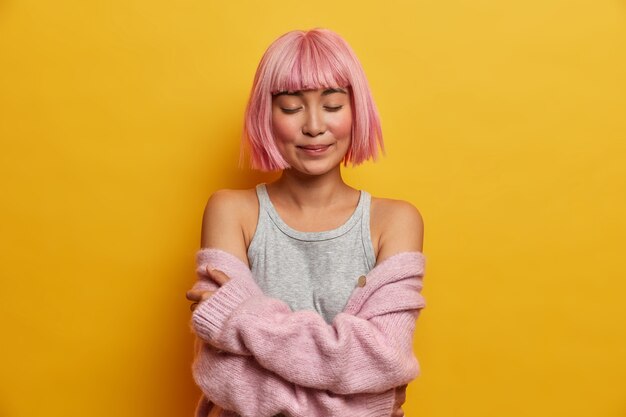 밥 헤어 스타일로 만족 한 여성의 사진, 분홍색 머리카락이 즐거움에서 눈을 감고 어깨에서 떨어진 부드럽고 따뜻한 스웨터를 입습니다.