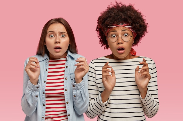 Photo of scared multiethnic women look with terror, notice something horrible, keep hands in protective gesture