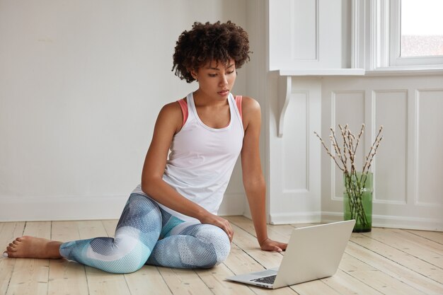 Photo of serious concentrated female fitness trainer watches tutorial video on laptop computer