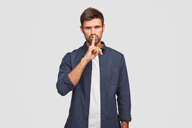 Photo of serious male keeps index finger on lips as demonstrates hush gesture