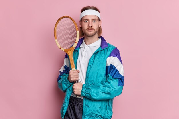 Photo of serious man holds tennis racket looks self assured dressed in sportsclothes brags about his sport achievements practices tennis skills achieved top. Match winner.