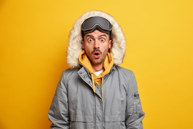 ショックを受けた男のスキーヤーの写真は、寒い冬の天候のために暖かい無言のドレスを凝視し、スキーゴーグルを着用します。