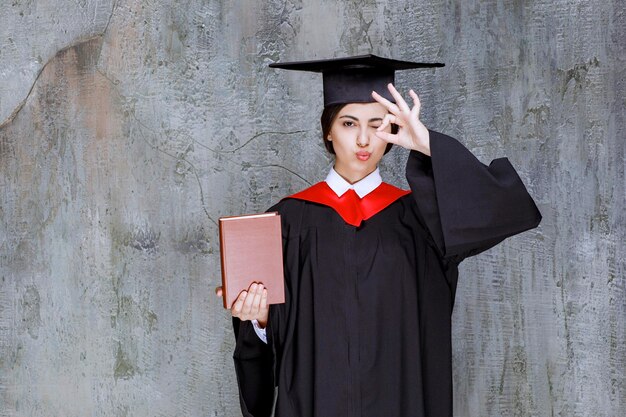 Photo of smart graduate student showing her diploma book over wall. High quality photo