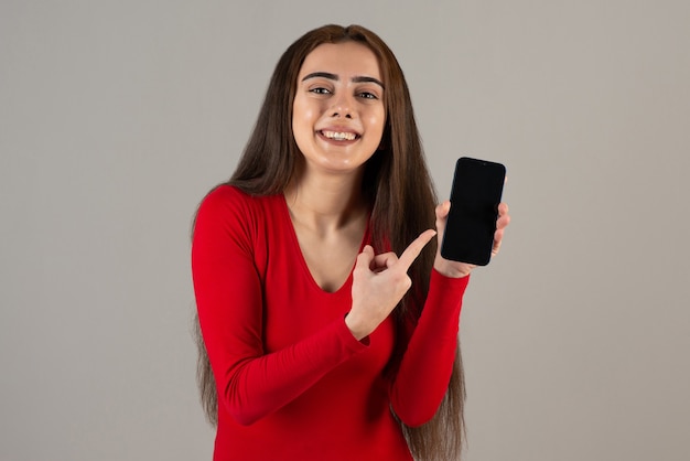 회색 벽에 핸드폰을 들고 빨간 운동복을 입은 사랑스러운 소녀가 웃고 있는 사진.