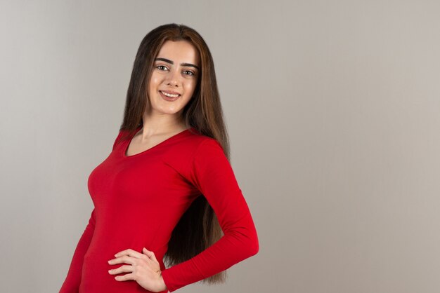 Photo of smiling adorable girl in red sweatshirt standing on gray wall.