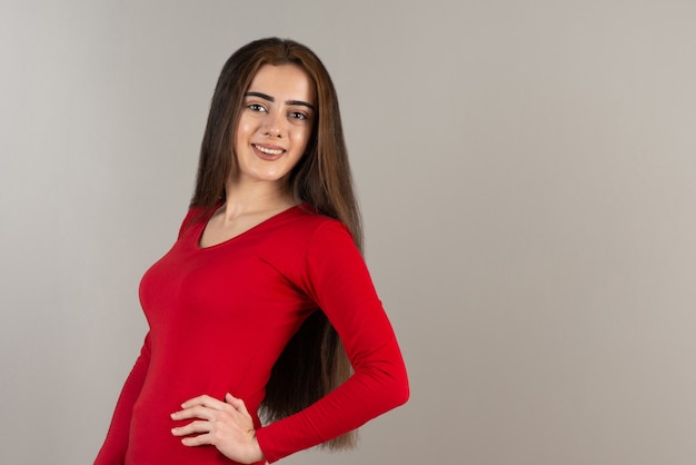 Photo of smiling adorable girl in red sweatshirt standing on gray wall.