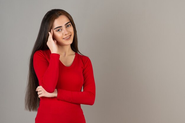 Photo of smiling adorable girl in red sweatshirt standing on gray wall.