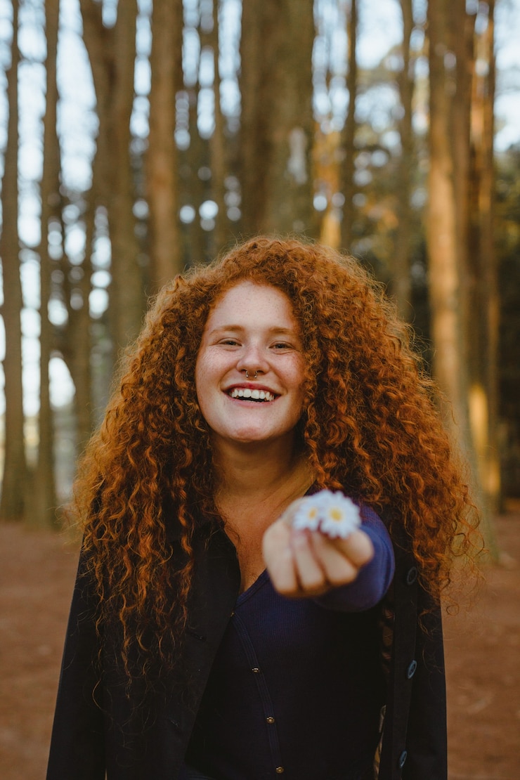 Free Photo photo of smiling woman posing while holding white daisy flowers in the forest