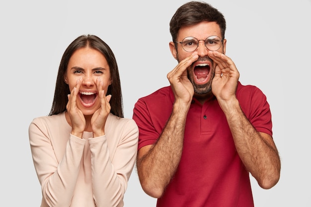 На фото стрессовые европейские женщина и мужчина громко восклицают, держат рот широко открытыми, кричат от злости на кого-то