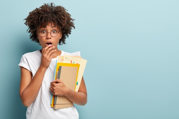 Photo of stupefied African American student going to have extra courses, gasps from surprisement, keeps hand on lips