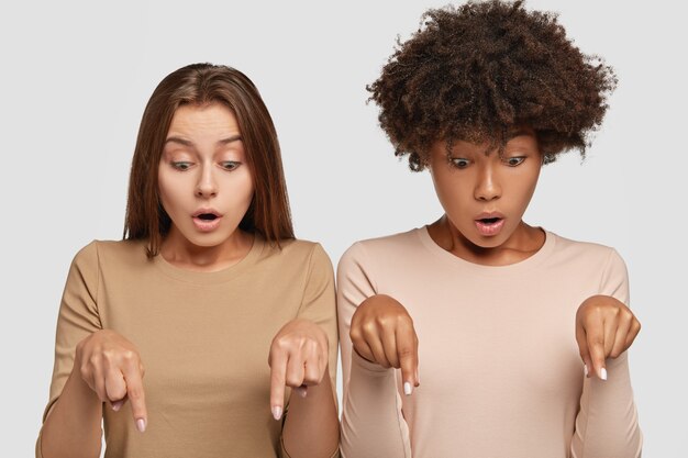 愚かな混血の若い白人女性が一緒に床を指差して、見下ろして驚いた写真