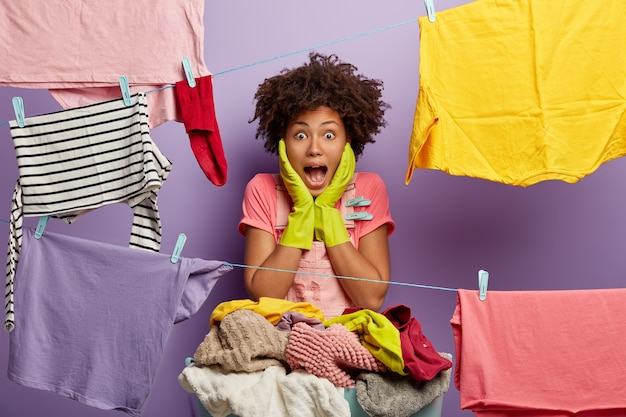 Free photo photo of surprised african american woman wears rubber protective gloves, keeps palms on cheeks