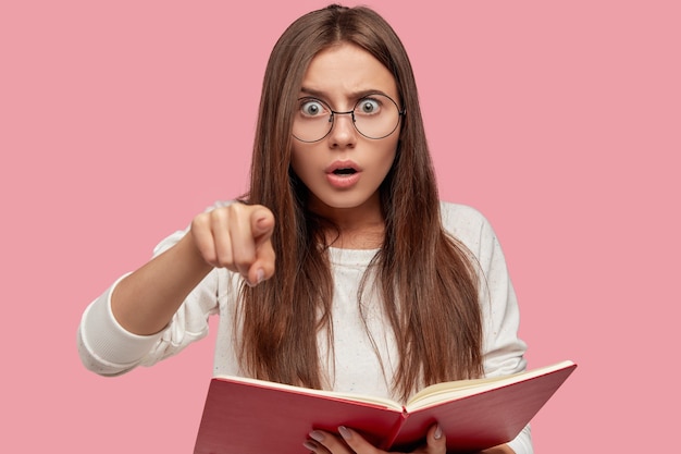 Photo of surprised brunette young European woman points with index finger directly 