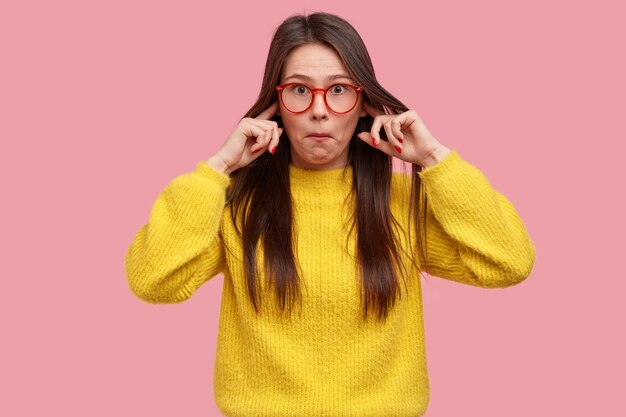 Photo of surprised lady cant stand terrible sound, surprised with rumors, pluggs ears, wears yellow clothes