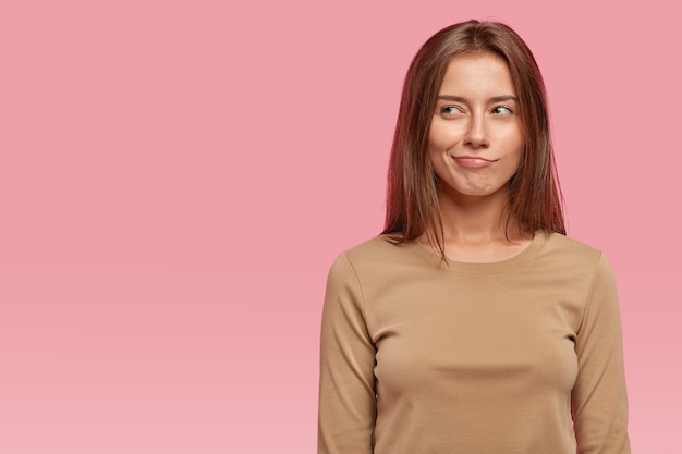 Photo of thoughtful contemplative young woman purses lips with mysterious expression