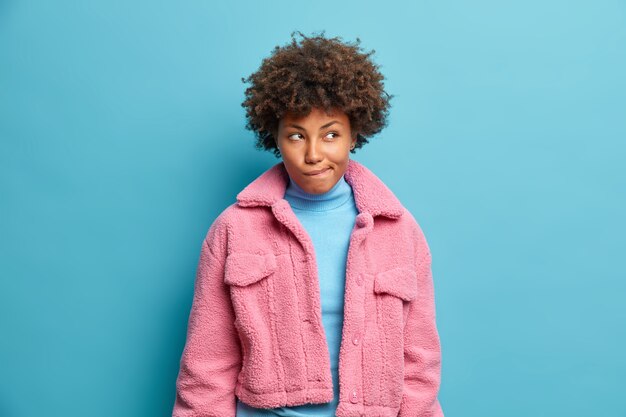 Photo of thoughtful dark skinned woman bites lips and looks away pensively has doubts