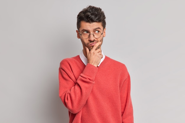 Photo of thoughtful handsome adult European man holds chin and looks pensively away tries to solve problem