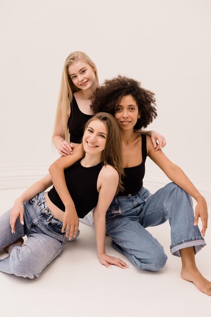 Photo of three young interracial women of light and dark hair in black top and jeans isolated on white background