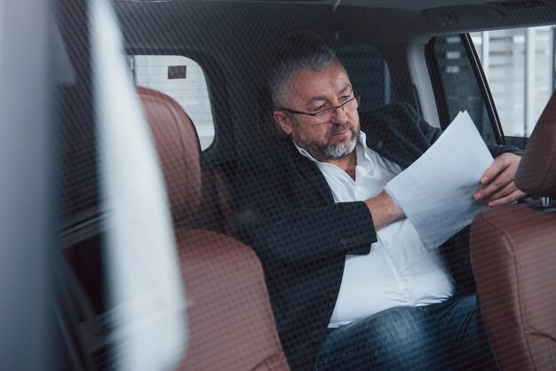 Photo through the glass. Paperwork on the back seat of the car. Senior businessman with documents