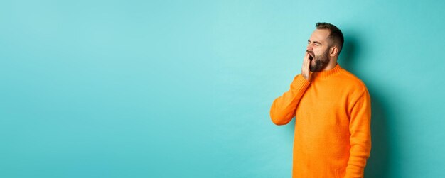 Photo of tired bearded man yawning cover mouth with hand standing sleepy against light blue backgrou