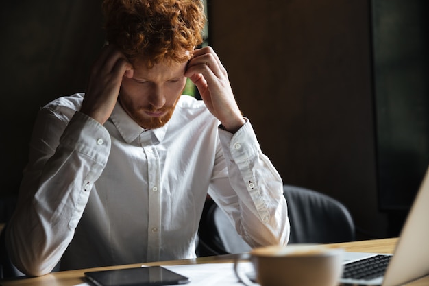 Free photo photo of tired redhead businessman, touching his head, looking at digital tablet