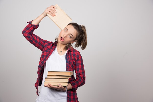 Photo of a tired young student holding a stack of books.