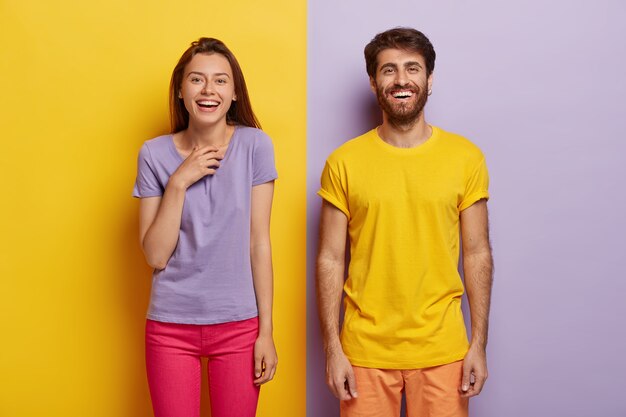 Photo of two delighted young woman and man stand together, express good emotions, smile happily