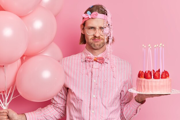 불행한 생일 남자의 사진은 파티에 기분이 좋지 않아 맛있는 케이크와 헬륨 풍선 무리를 보유하고 있습니다.