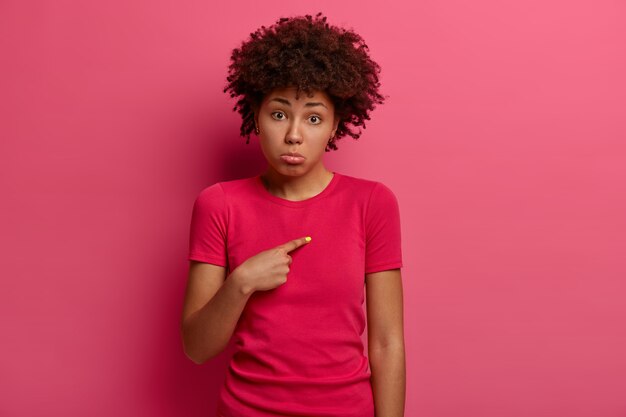 不幸な若いアフリカ系アメリカ人女性の写真は、悲惨な表情で自分自身を指さし、なぜ私が罪を犯しているのかと尋ね、悪い感情から下唇を財布に入れ、深紅色のTシャツを着て、悲しい言及されています