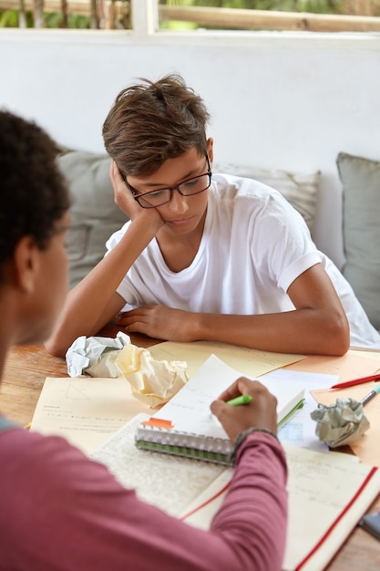 Photo of unrecognizable lady sits back, points with pen in notebook, explains material to younger brother, pose at workplace, helps with financial report, gives assistant, explains task