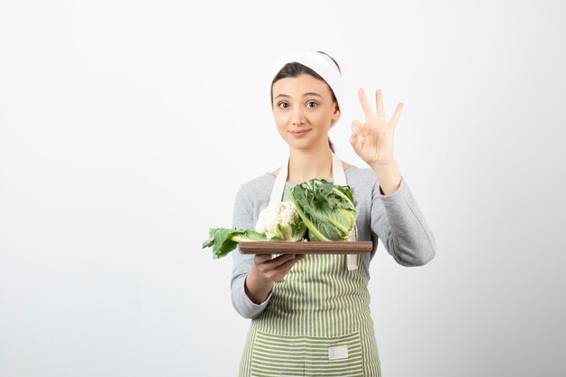 Photo of a woman in apron with a wooden plate of cauliflowers showing ok gesture