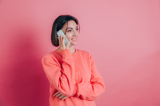 Photo of woman smiling while talking on smartphone isolated over pink background