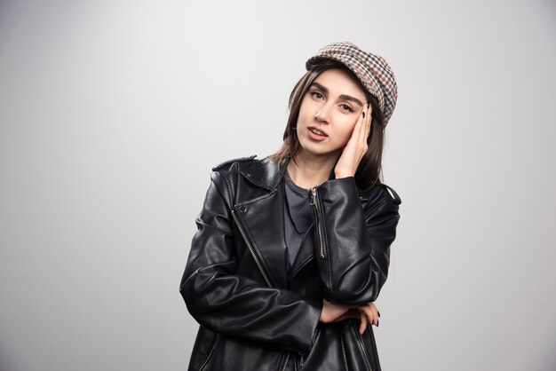 Photo of a woman touching her head in black leather jacket and cap.