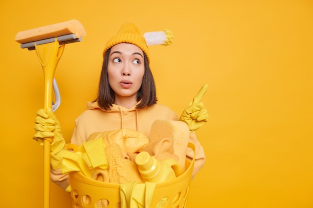 복사 공간에 멀리 궁금 아시아 여자 포인트의 사진은 노란색 배경 위에 절연 바쁜 토요일 동안 세탁을 청소 용품 포즈 뭔가 보여줍니다. 가사 개념