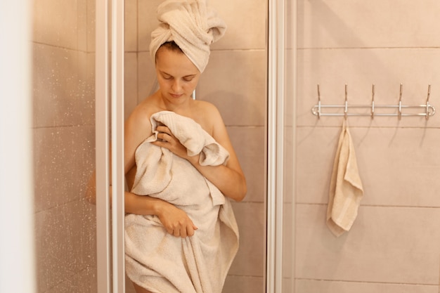 Photo of young adult slim beautiful woman getting out of the shower, standing and drying the body with a towel, taking shower in the morning, cleanliness.