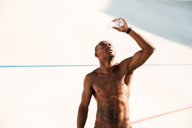 Фотография молодого африканского спортивного человека, льющего воду на его голову