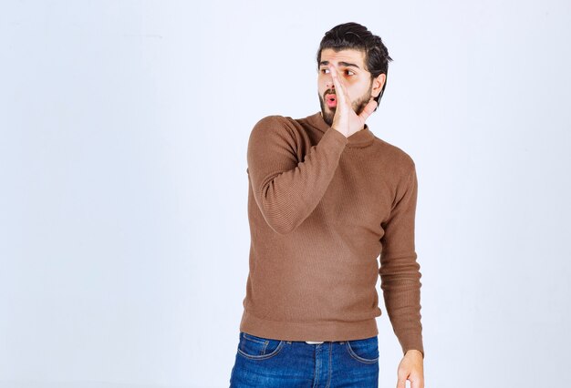 Photo of a young attractive man model standing and looking away over white wall. High quality photo