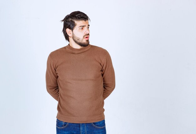 Photo of a young attractive man model standing and looking away over white wall. High quality photo